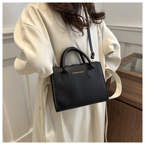 Detail of black leather tote bag with wavy edges and gold fashion text lettering