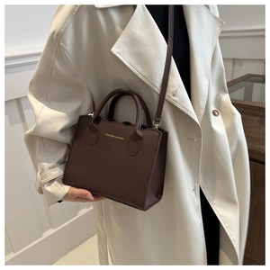 Detail of dark coffee PU leather tote bag with gold lettering shown on a trench coat