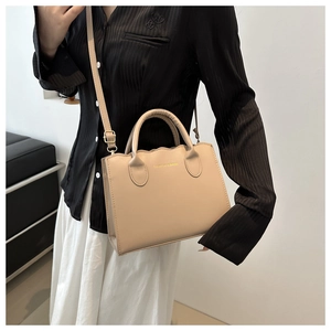 Beige wavy-edge crossbody tote bag shown on model with gold fashion lettering
