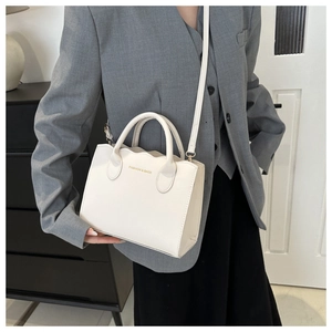 Detail of wave-edged white crossbody bag with gold fashion text and slim shoulder strap