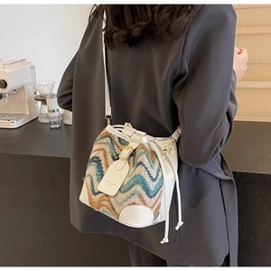 Close-up of wavy texture fabric and leather on bucket bag with gold metal buckle