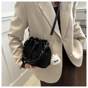 Detail of black suede bucket bag featuring woven handle and cute cat plush charm