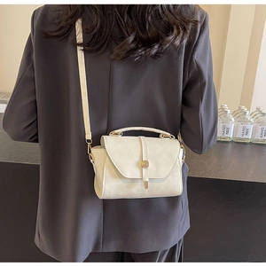 Gros plan d'un petit sac carré crème rétro avec boucle dorée sur un blazer gris chic