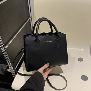 Black wavy edge crossbody tote bag in matte leather with gold lettering and shoulder strap