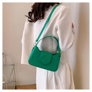 Détail du sac bandoulière vert vif avec texte doré sur une tenue de blazer blanc