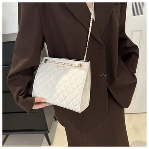 Gros plan d'un sac bandoulière blanc matelassé avec chaîne sur un blazer marron chic