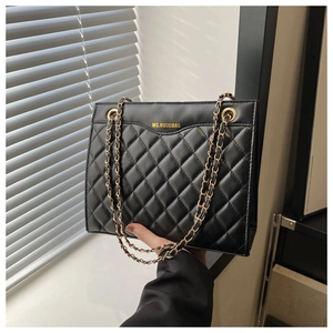 Détail de la texture matelassée noire et de la bandoulière chaîne dorée sur un sac élégant
