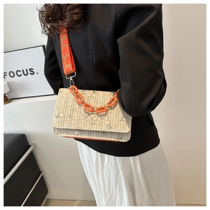 Detail of embroidered straw crossbody bag with orange chain and wide jacquard strap