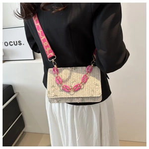 Detail view of woven straw crossbody bag featuring floral embroidery and wide pink shoulder strap