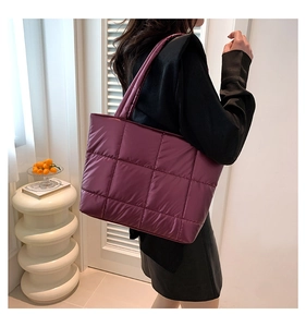 Detail of a large purple quilted puffer tote bag in glossy nylon on a model