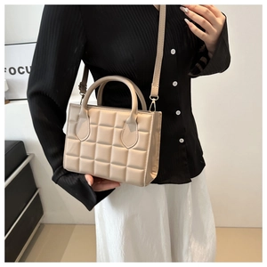 Detail of cream crossbody bag with plaid embossing held by hand in casual setting