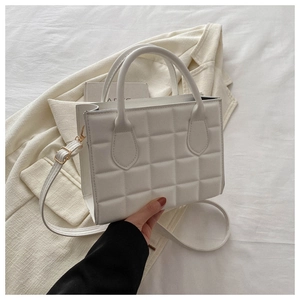 Detail of white quilted crossbody bag with golden hardware and textured grid pattern