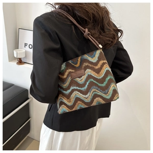 Detail of striped knit bucket bag with brown leather knotted strap on a model's shoulder