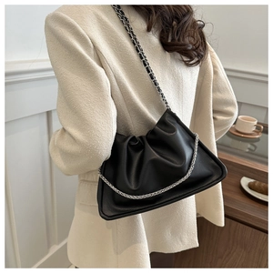 Detail of a black ruched shoulder bag with a silver chain strap worn on a beige blazer