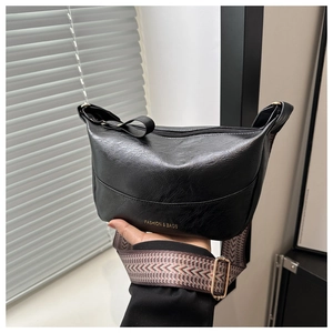 Detail of black faux leather crossbody bag with wide jacquard strap and gold lettering
