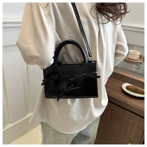 Detail shot of black bow-knot crossbody bag worn with a casual outfit in a cozy cafe