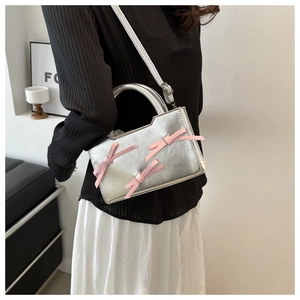 Détail du sac à main argenté avec nœuds roses porté par un mannequin pour un look tendance