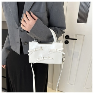 Close-up of white crossbody bag with bow accents and top handle held by a model