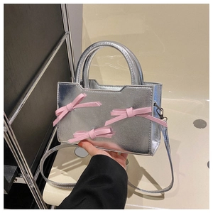 Détail du sac carré en cuir verni argenté avec trois nœuds roses et poignée rigide