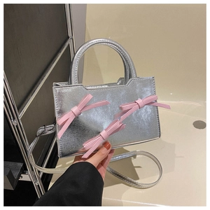 Détail du sac à main en cuir verni argenté avec nœuds roses et bandoulière