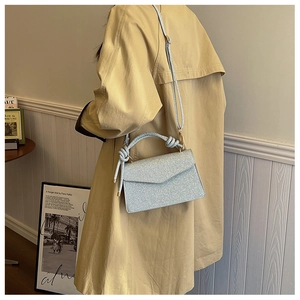 Detail of light blue glitter crossbody bag with knot handle worn by a model