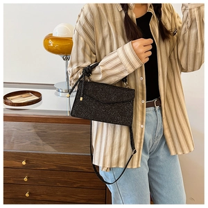 Detail of a vintage black glitter crossbody bag shown on a model in a retro setting