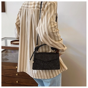 Detail of black glitter crossbody bag featuring knot handle design and gold hardware