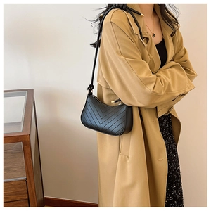Dettaglio borsa a spalla nera trapuntata a V con finiture dorate e trench coat kaki