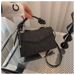 Close-up of black glitter handbag featuring a knotted handle and gold metal hardware