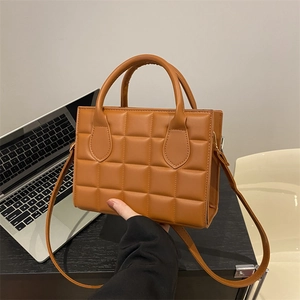 Brown quilted square handbag with adjustable shoulder strap on a desk with a laptop
