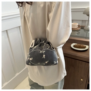 Detail of dark grey embroidered drawstring bucket bag worn cross-body in a cozy indoor setting