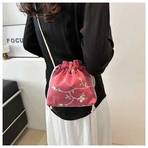 Detailed embroidery of white flowers on a magenta drawstring crossbody bucket bag
