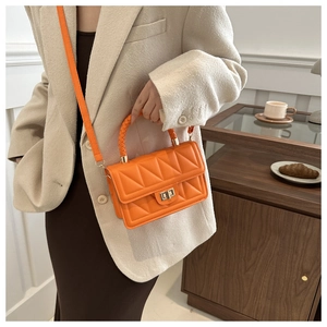 Detail of orange quilted crossbody bag with metal twist lock and woven handle held by model