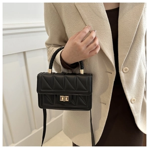 Detail of black quilted crossbody bag featuring golden lock and woven handle
