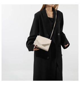 Détail du sac matelassé ivoire avec chaîne dorée porté sur un blazer noir chic