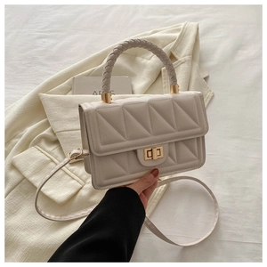 Detail of cream flap bag with quilted patterns, woven handle and gold twist lock