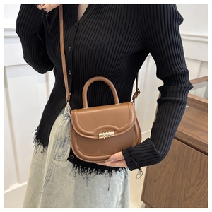 Detail of a brown saddle bag with golden metal hardware and a retro top handle design