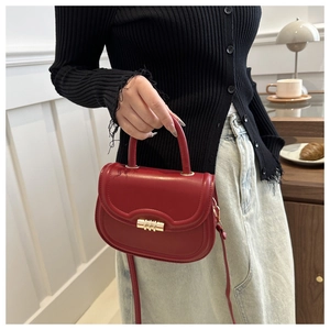 Detailed view of a red leather saddle bag with gold cylindrical buckle and shoulder strap