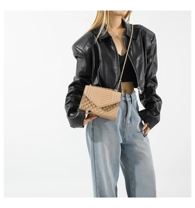Détail d'un sac bandoulière beige matelassé avec chaîne dorée porté par un mannequin