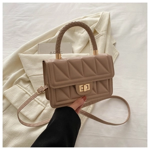 Close-up of khaki quilted crossbody bag with golden twist lock on a beige blazer