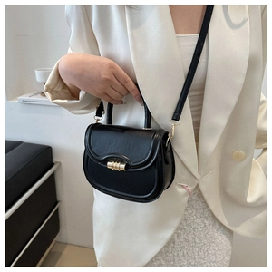 Detail view of black saddle bag with gold metal clasp on a model in white blazer