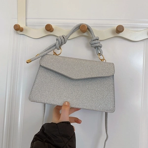Silver sequin crossbody flap bag with knot handle held against a minimalist background