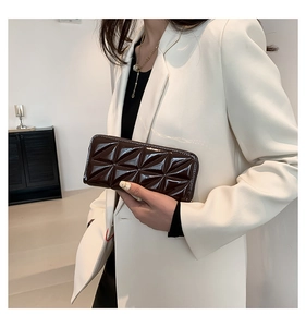 Detail of dark brown quilted leather long wallet held by a model in a white suit