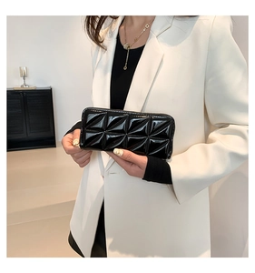 Détail de la pochette noire en cuir verni matelassé avec motif élégant de losanges