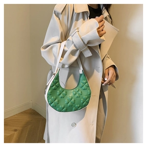 Detail of green crescent shoulder bag with embossed clover texture and white strap contrast