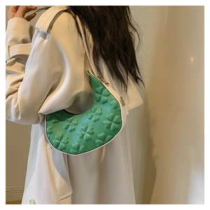 Detail of green crescent shoulder bag with 3D clover embossing worn by model