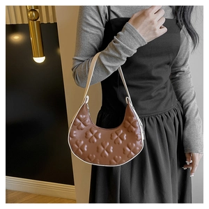 Close-up of brown crescent underarm bag featuring embossed clover texture and white handle