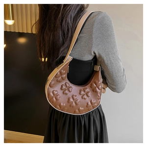 Detail of embossed clover pattern on a brown leather half-moon shoulder bag for women