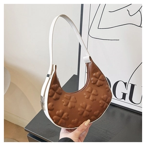 Detailed macro of the four-leaf clover embossed texture on the brown and white shoulder bag