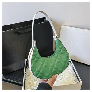 Detail of green hobo bag with embossed clover pattern and white strap in a gift box